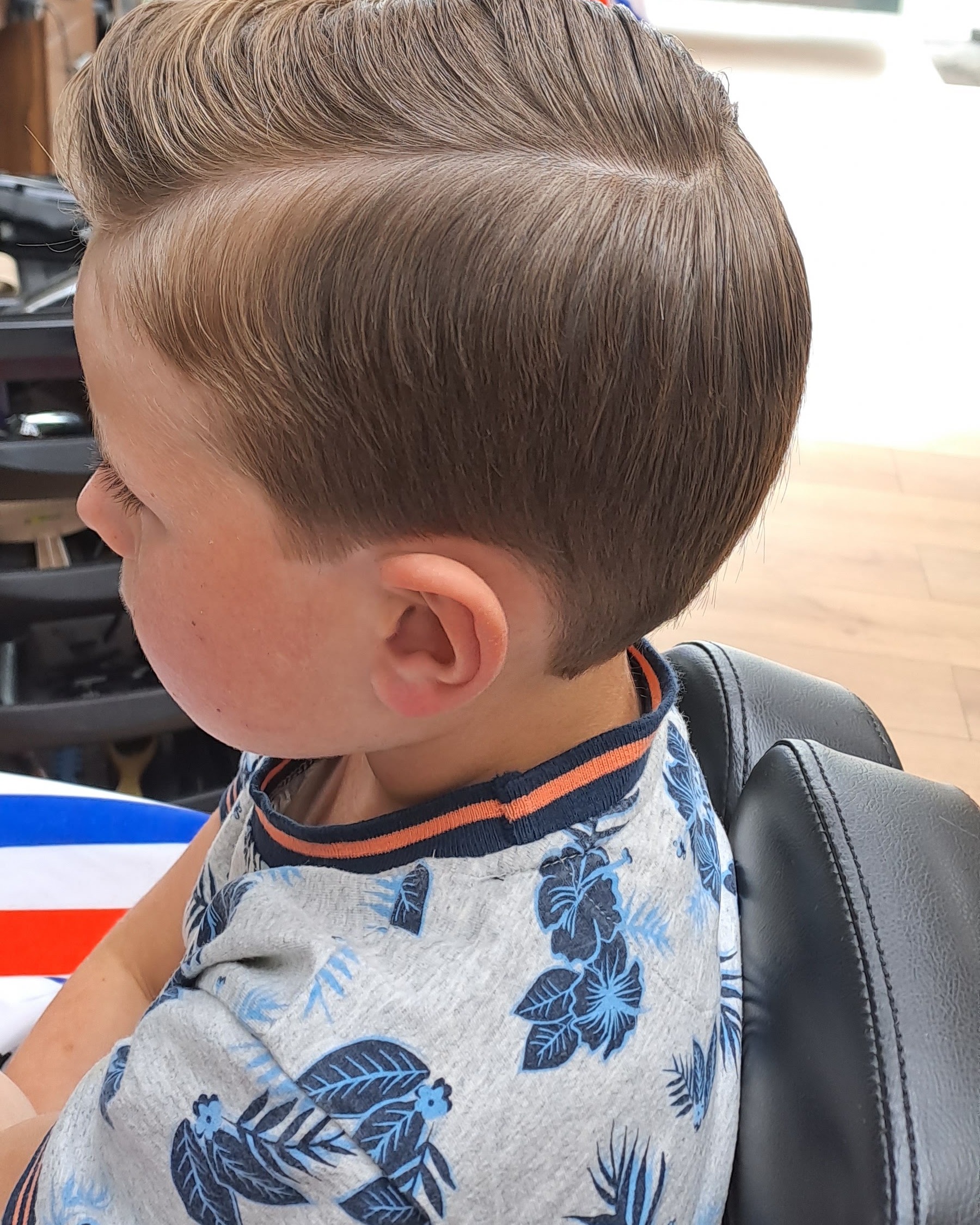 Een jongen met een net geknipt kapsel met scheiding, in profiel bij het raam van de salon