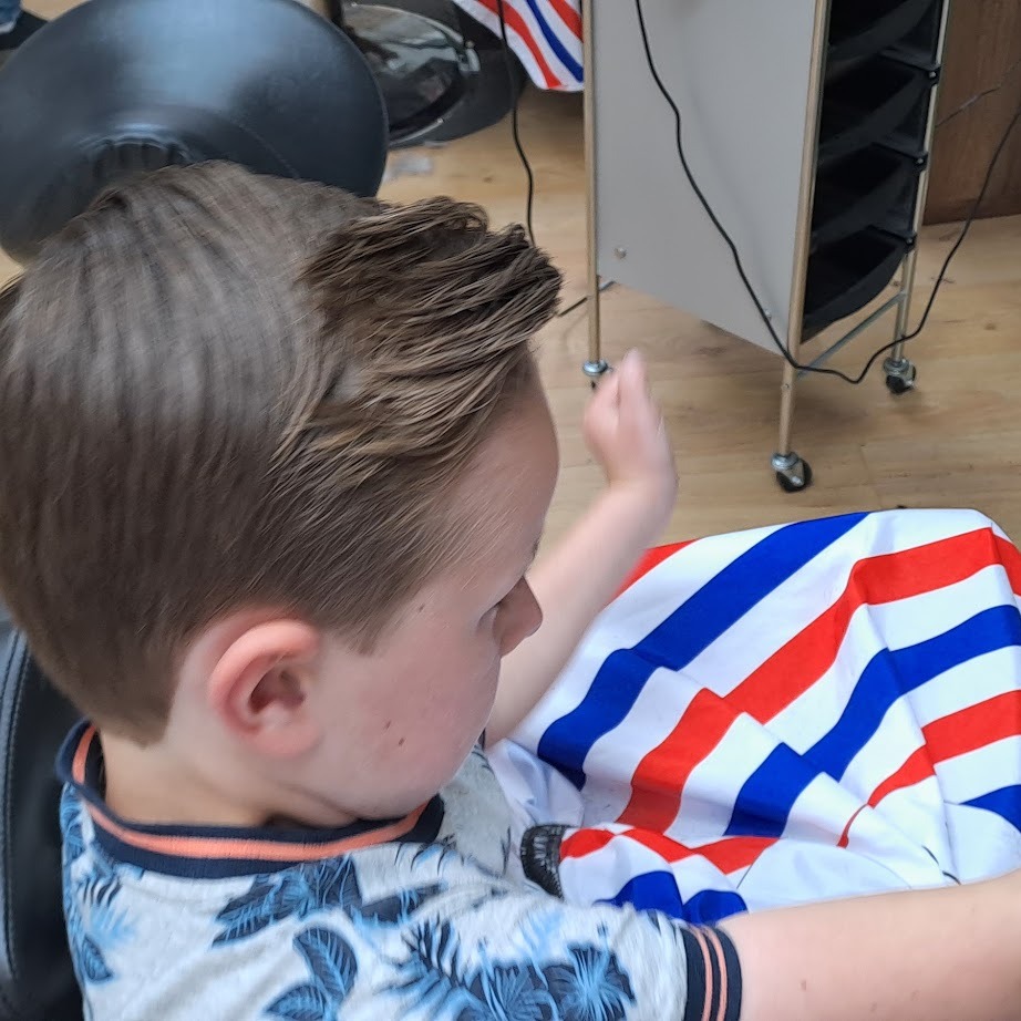 Een jongen in de kappersstoel met een gestreepte kapmantel, net geknipt
